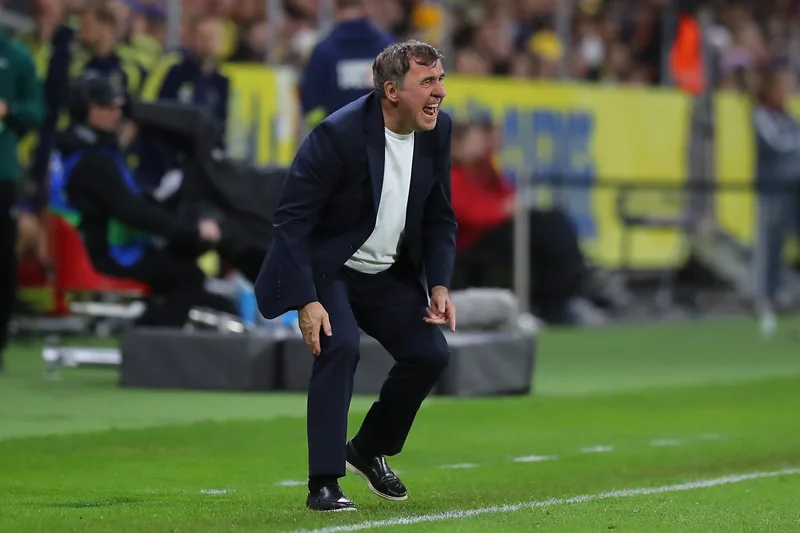 Bărbat în costum ghemuit pe marginea terenului, la meciul de fotbal România-Suedia