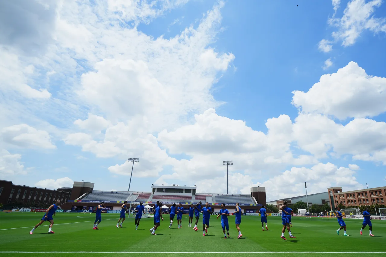 Fotbaliști în echipament albastru la antrenament, pe un teren sub un cer cu nori albi