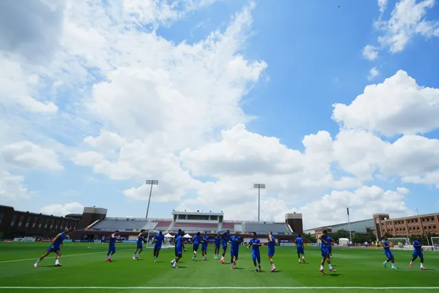 Fotbaliști în echipament albastru la antrenament, pe un teren sub un cer cu nori albi