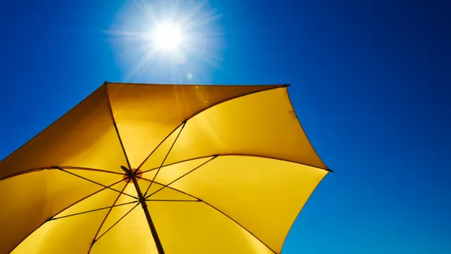 Umbrelă galbenă sub soarele puternic, pe un cer albastru senin