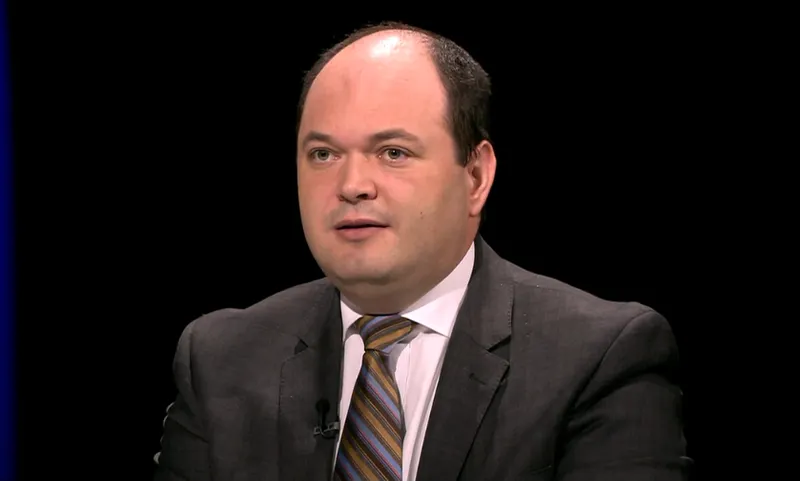 Bărbat cu părul rărit, în costum și cravată cu dungi, într-un studio cu fundal negru