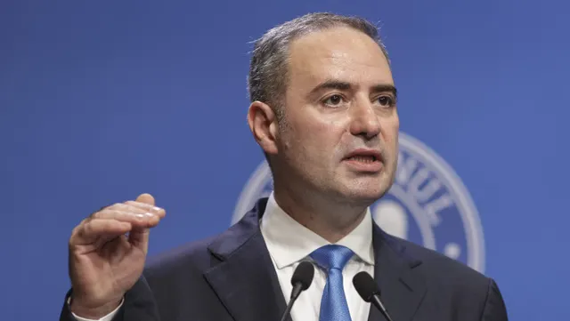 Bărbat în costum, cu cravată albastră, gesticulând la microfoane, în fața siglei Guvernului