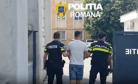 Doi polițiști escortând un tânăr în tricou alb, cu sigla Poliției Române în colț
