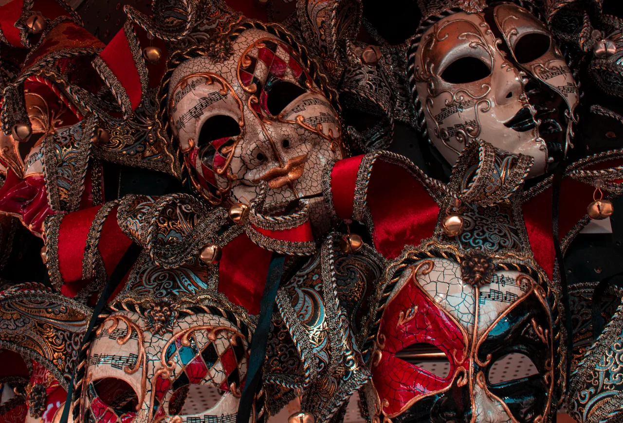 Măști venețiene de carnaval, ornamentate în roșu, auriu și alb, așezate unele lângă altele
