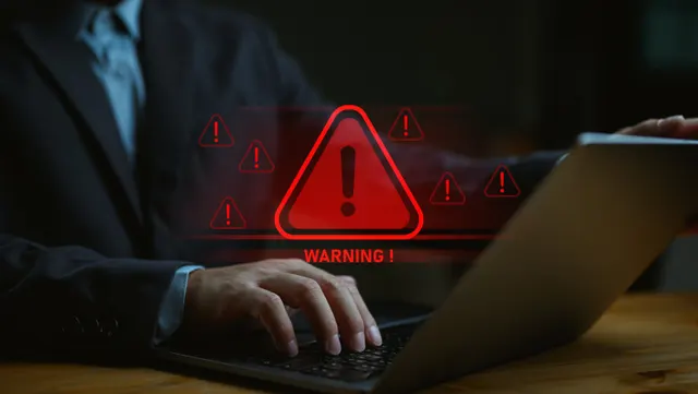 Bărbat în costum la un laptop, cu semne roșii de avertizare și textul „Warning!” deasupra tastaturii