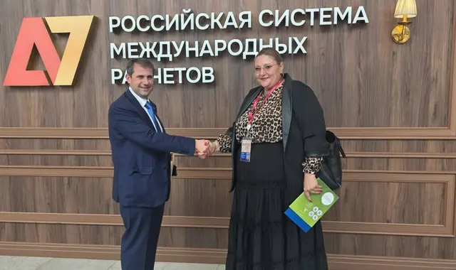 Ilan Șor și Diana Șoșoacă dând mâna în fața unui panou în rusă al Sistemului rusesc de decontări internaționale