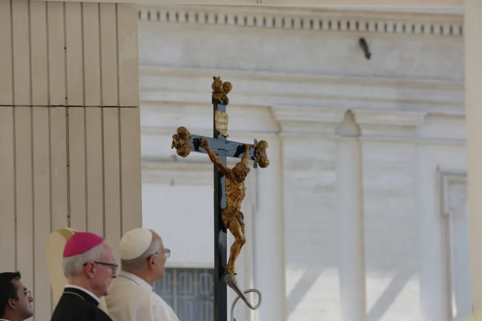 Doi clerici catolici, unul în veșmânt alb și unul cu calotă violet, lângă un crucifix