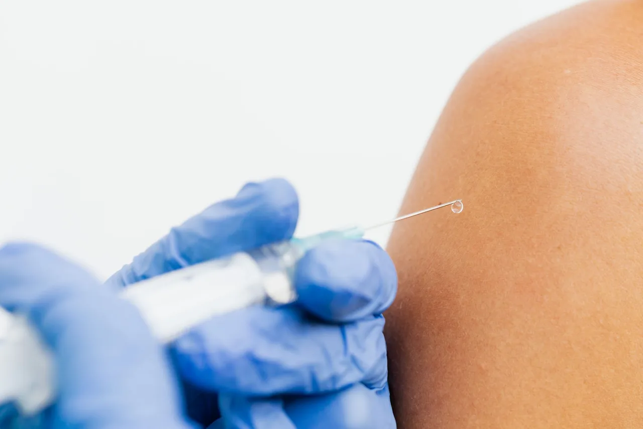 Mână cu mănușă albastră care face o injecție în brațul unei persoane