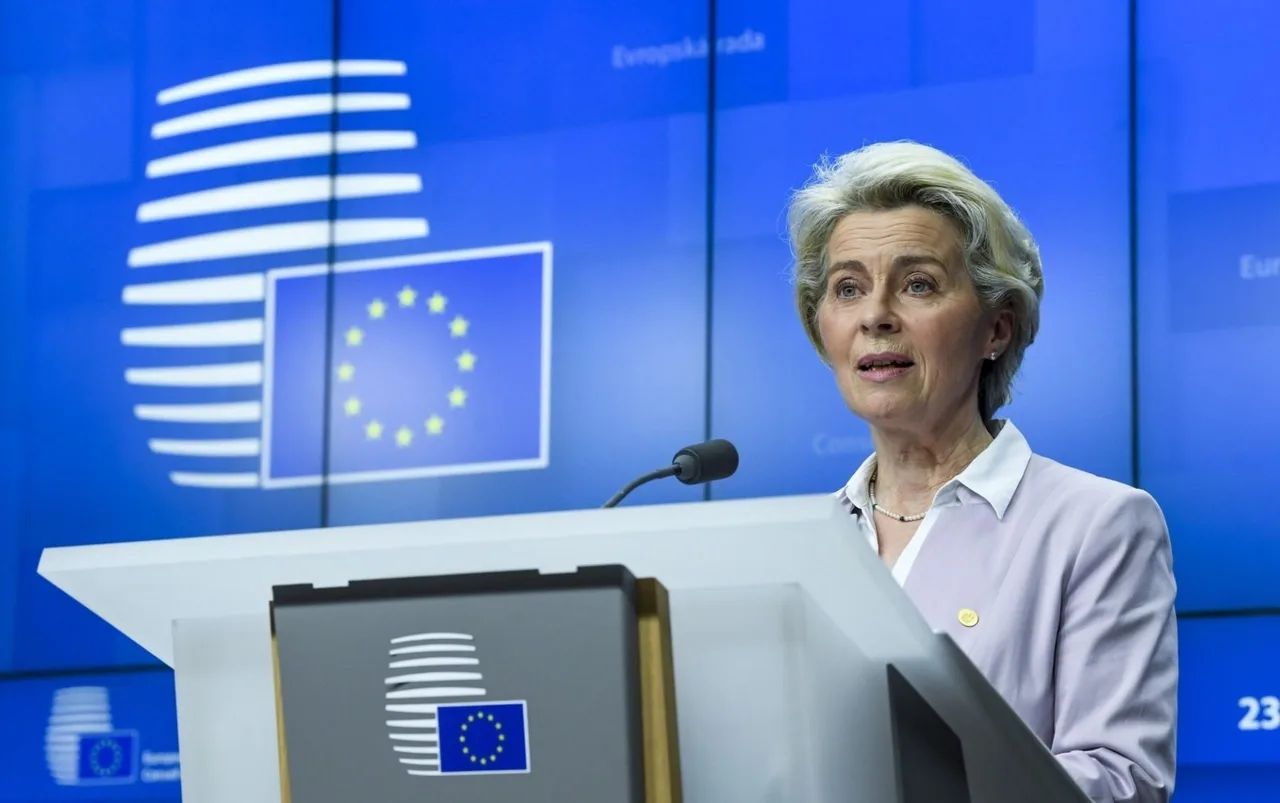Femeie cu părul blond, în sacou lila, vorbind la un pupitru, pe fundal albastru cu sigla UE