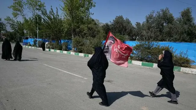Femei în veșminte negre traversând o stradă lângă un parc, sub cer senin