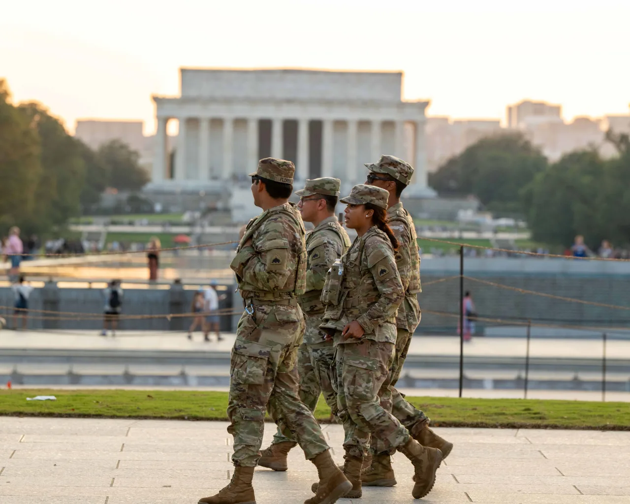 Trei militari în uniforme de camuflaj mergând pe aleea din fața Memorialului Lincoln din Washington