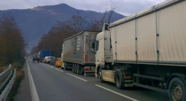 Coloană de camioane oprite pe un drum de pe Valea Oltului, cu munții în fundal