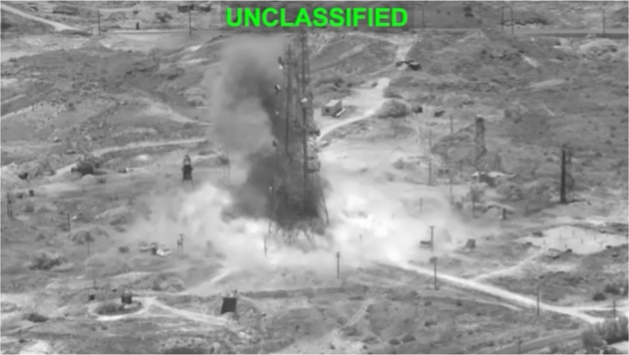 Captură alb-negru dintr-o filmare aeriană militară, cu o explozie lângă o structură și mențiunea „UNCLASSIFIED”