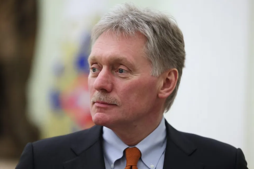 Dmitri Peskov, cu părul grizonat și mustață, în costum și cravată portocalie