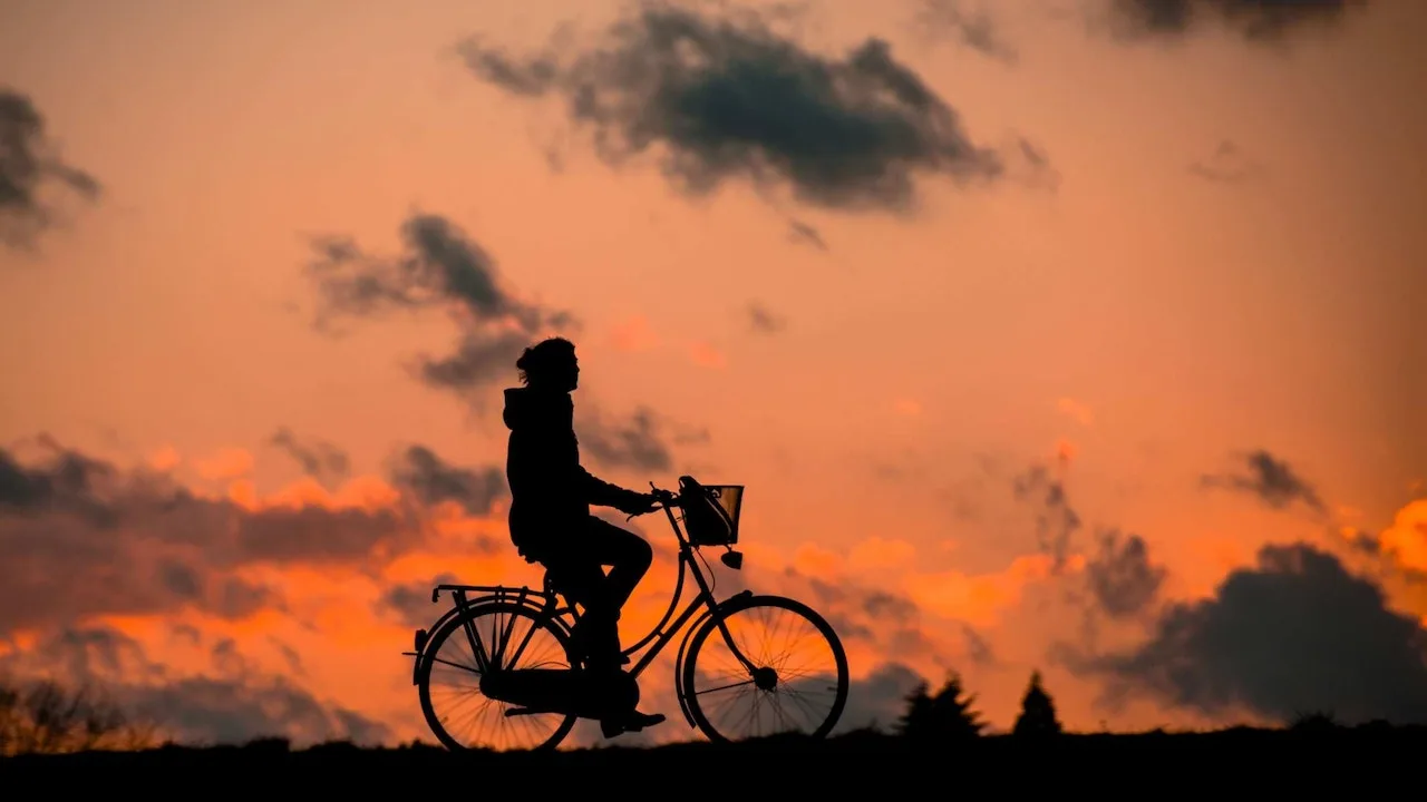 Silueta unui biciclist pe fundalul unui cer portocaliu la apus