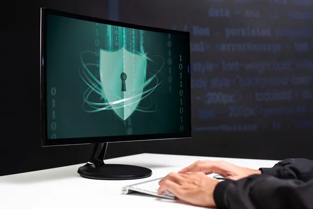 Monitor cu un scut cu gaura cheii pe ecran și mâinile cuiva pe tastatură