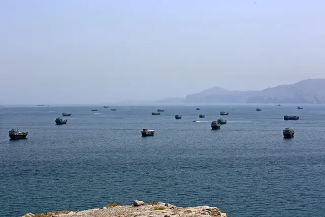 Zeci de nave ancorate pe o mare liniștită, în apropierea unei coaste cu dealuri