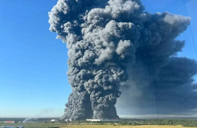 Coloană uriașă de fum negru ridicându-se de la un incendiu, deasupra unei câmpii