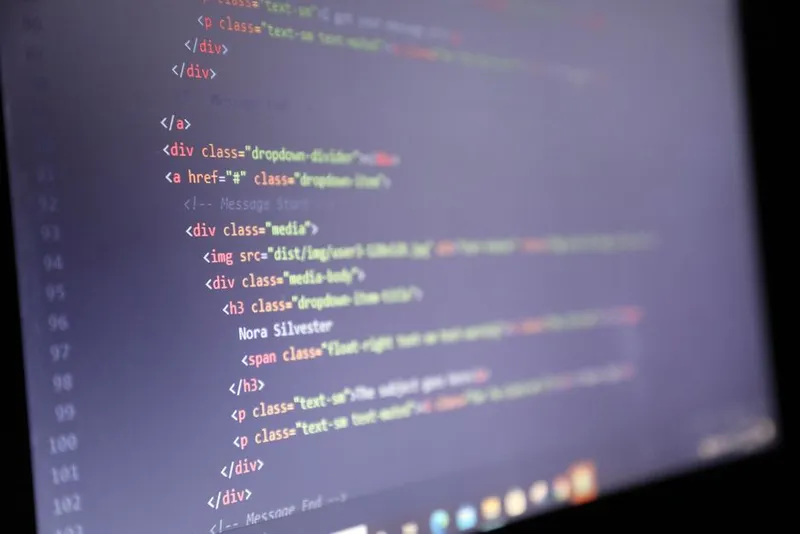 Ecran de laptop cu cod HTML, văzut din unghi, în lumină slabă