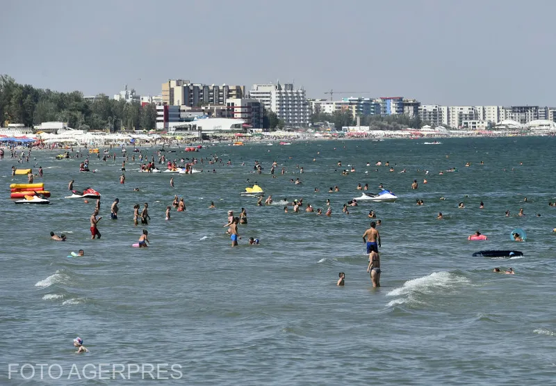 Turiști în mare și pe plajă, cu hotelurile stațiunii Mamaia în fundal