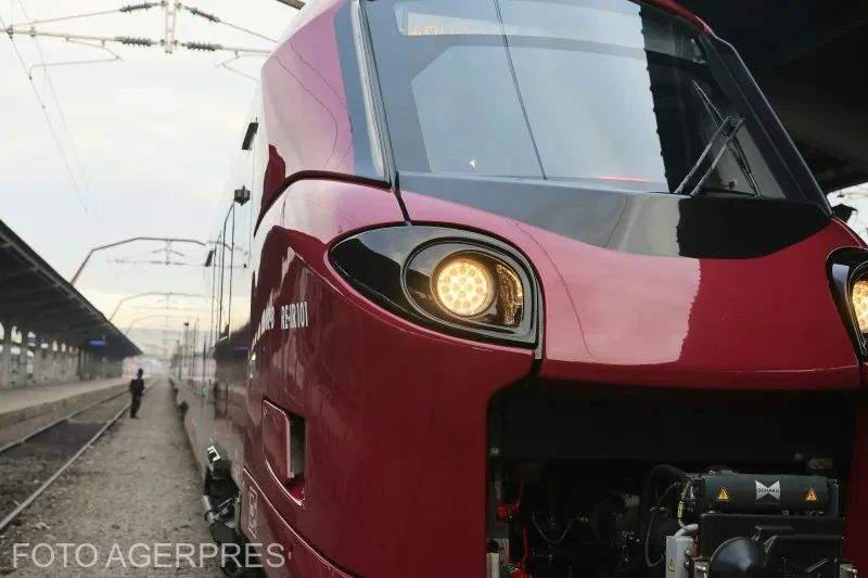 Tren electric Alstom roșu, oprit lângă un peron, cu farurile aprinse