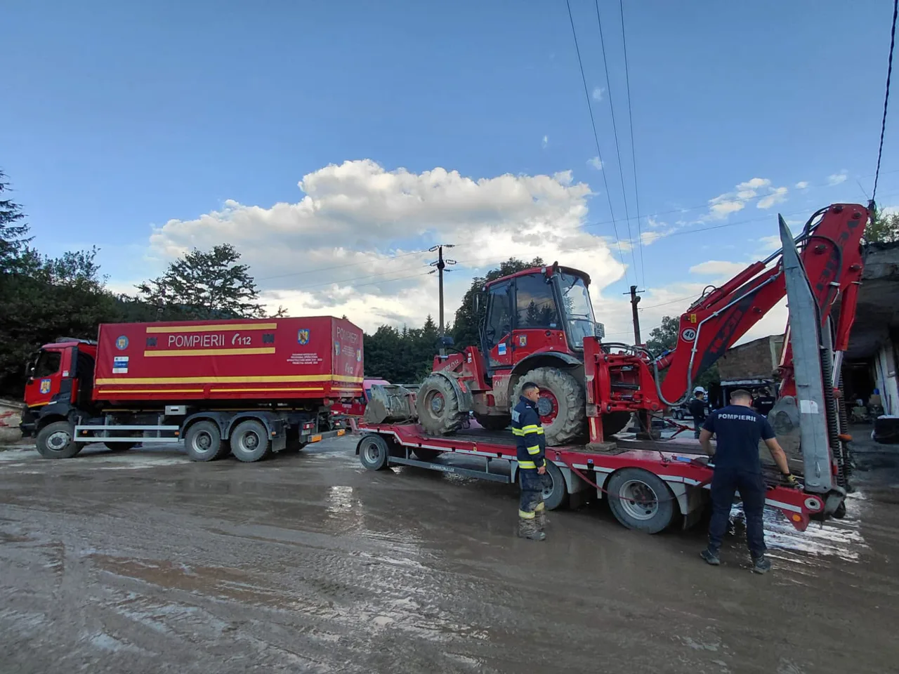 Autospecială de pompieri și un excavator pe o stradă acoperită de noroi, după o inundație
