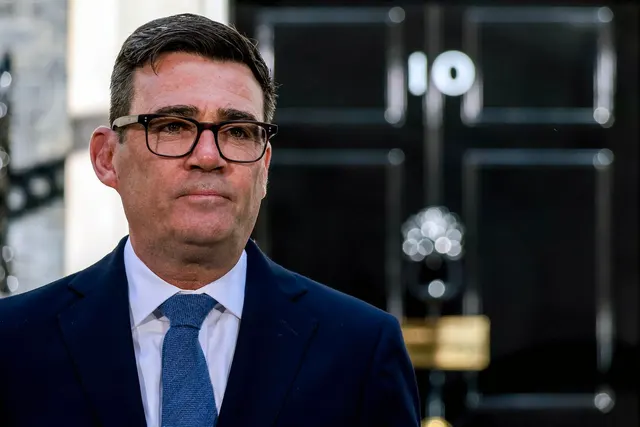 Bărbat cu ochelari, în costum și cravată albastră, în fața ușii de la Downing Street nr. 10