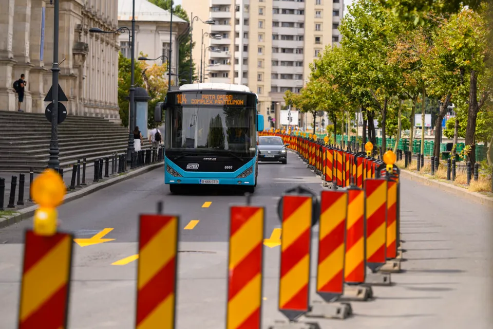 Autobuz albastru pe un bulevard, lângă un șir de separatoare de drum roșu cu alb