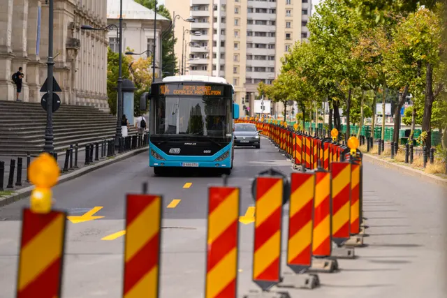 Autobuz albastru pe un bulevard, lângă un șir de separatoare de drum roșu cu alb
