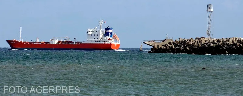 Navă cisternă cu cocă roșie lângă un dig de piatră cu far, pe mare