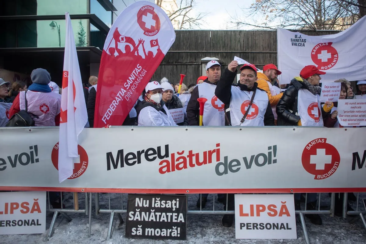 Protestatari Sanitas cu steaguri, în spatele bannerului „Mereu alături de voi!” și al pancartelor „Lipsă personal”