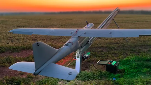 Dronă de recunoaștere albă pe o rampă de lansare, într-un câmp, la apus
