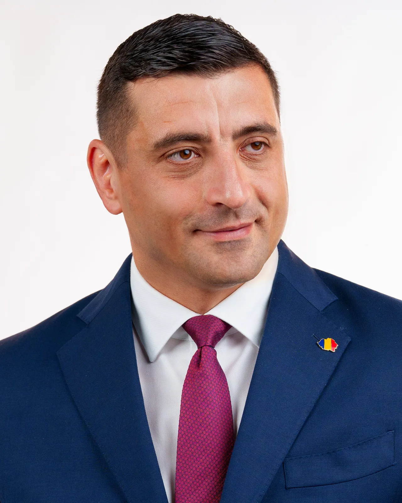 Portretul lui George Simion, în costum albastru și cravată roșie, pe fundal alb