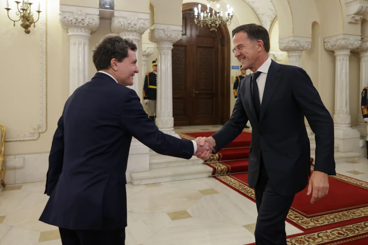 Doi bărbați în costume dându-și mâna pe un covor roșu, într-un hol cu coloane albe