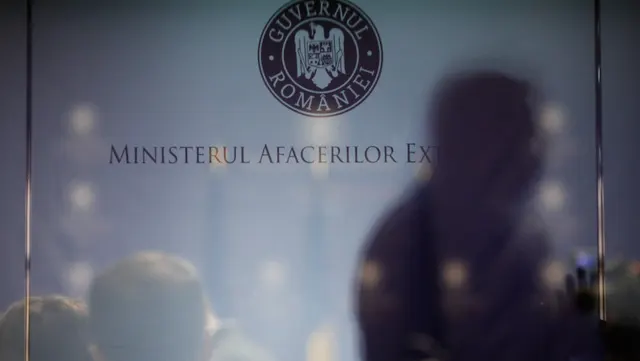Silueta estompată a unei persoane în fața inscripției „Ministerul Afacerilor Externe” și a stemei Guvernului