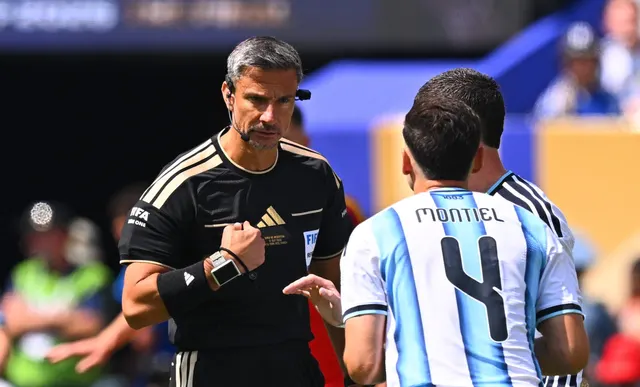 Arbitru în echipament negru vorbind cu un jucător al Argentinei care poartă numele Montiel și numărul 4