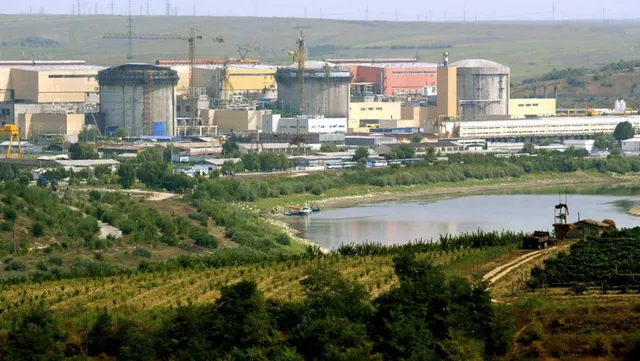 Centrală nucleară cu clădiri cilindrice, văzută peste un lac și dealuri cu vii