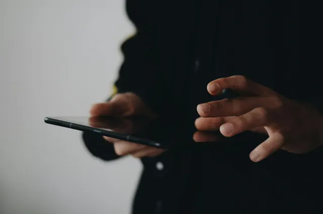 Mâini care țin un telefon mobil, pe un fundal întunecat