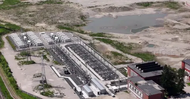 Vedere aeriană asupra unui teren industrial, cu o stație electrică, clădiri și un iaz