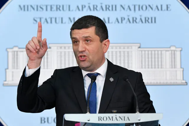 Bărbat cu degetul arătător ridicat, la pupitrul Ministerului Apărării Naționale
