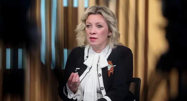 Femeie cu părul blond, în sacou negru cu panglica Sfântului Gheorghe, vorbind într-un studio
