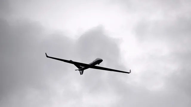 Dronă cu aripi lungi zburând pe un cer cenușiu, înnorat