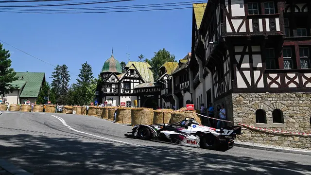 Mașină de curse pe o stradă în pantă din Sinaia, printre baloți de paie și clădiri cu căpriori