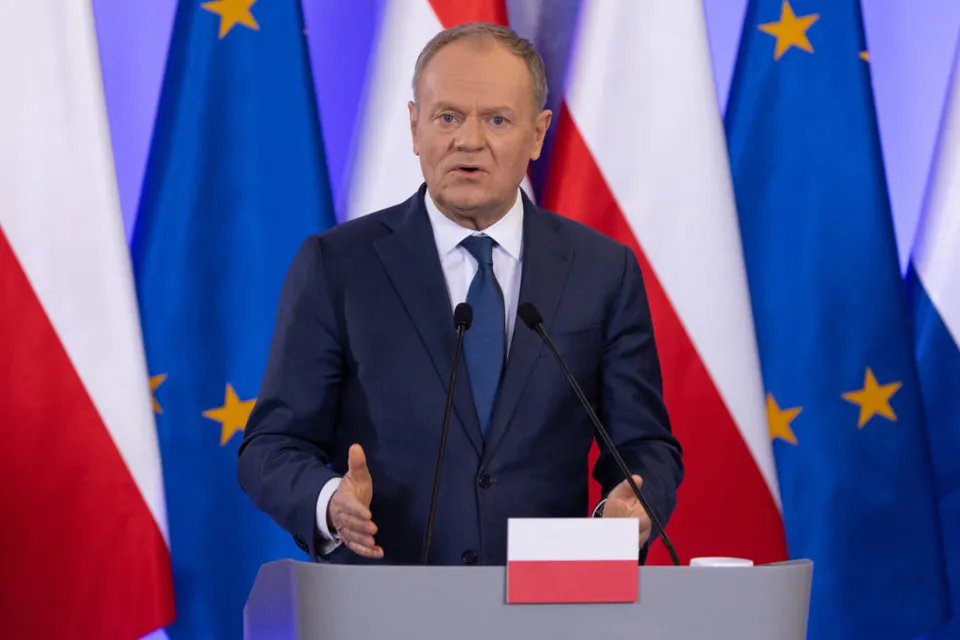 Donald Tusk vorbind la un pupitru, între drapelele Poloniei și ale Uniunii Europene