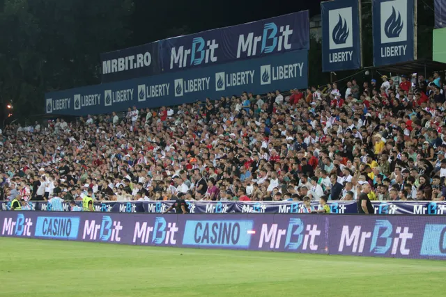 Tribună plină de suporteri pe un stadion, sub panourile publicitare MrBit și Liberty