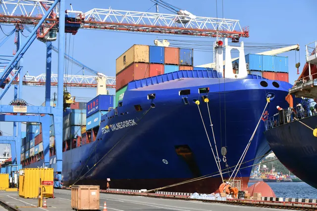 Navă portcontainer cu cocă albastră, încărcată cu containere, la cheiul unui port cu macarale