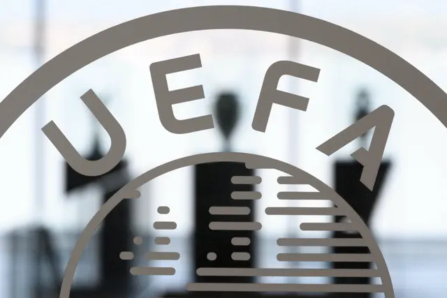 Sigla UEFA pe un geam, cu siluetele unor oameni în spate