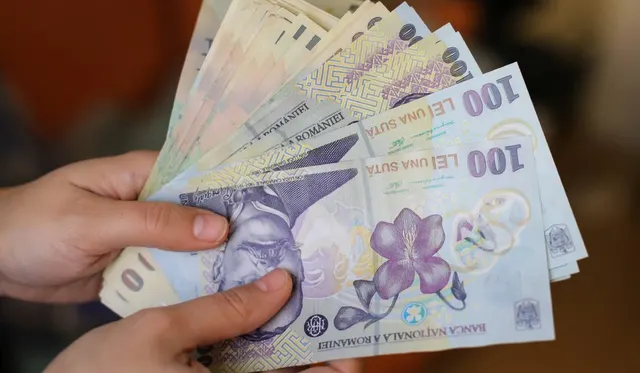 Mâini care țin un evantai de bancnote de 100 de lei