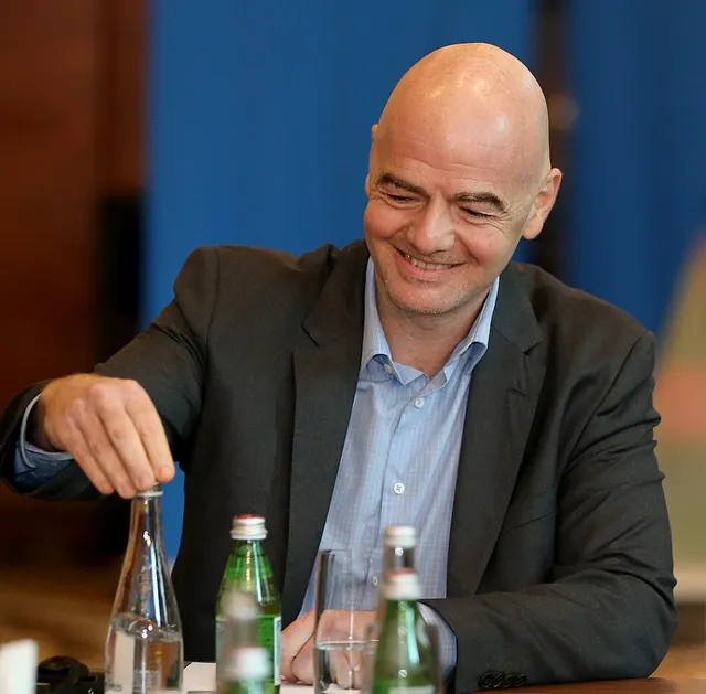 Gianni Infantino zâmbind, așezat la o masă cu sticle de apă