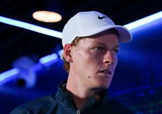 Jannik Sinner, cu o șapcă albă Nike, privind într-o parte, pe un fundal cu lumini albastre